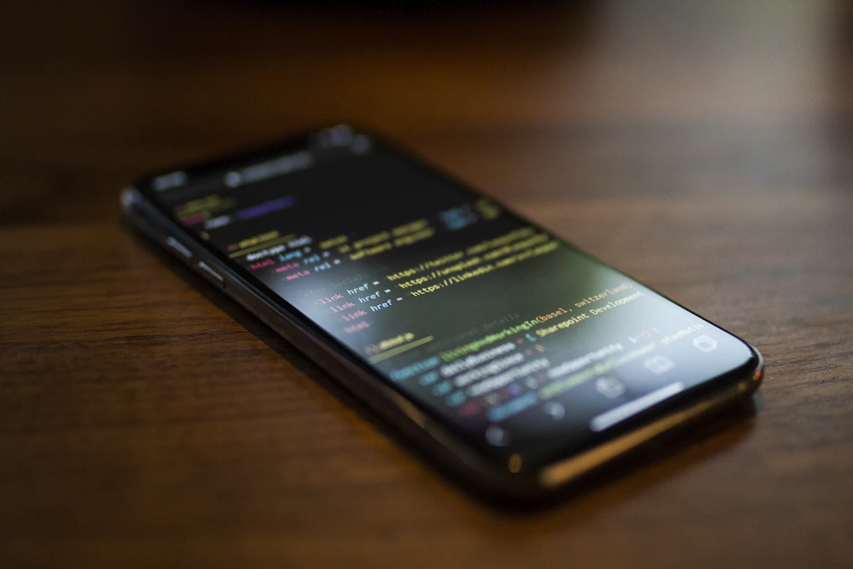 Smartphone lying on a wooden table with lines of code on its screen